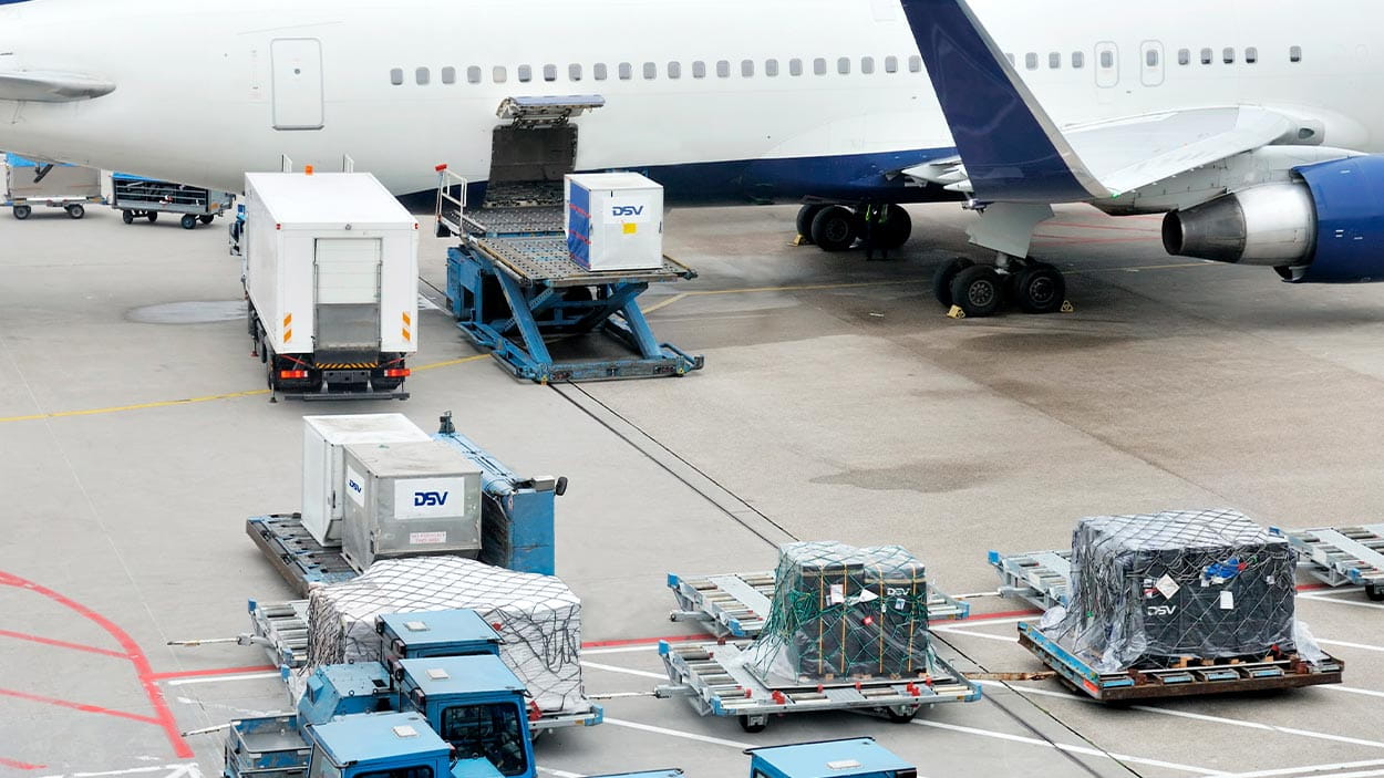 Cargo loading operations at an airport with an aeroplane, trucks, and DSV containers.